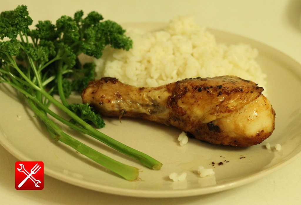 Полностью готовая жареная с чесноком куриная ножка на тарелке серверованная зеленью петрушки и рисом.