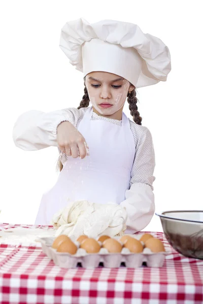 Маленькая девочка в белый фартук и шапку шеф-повара Замесить тесто в го Стоковая Картинка