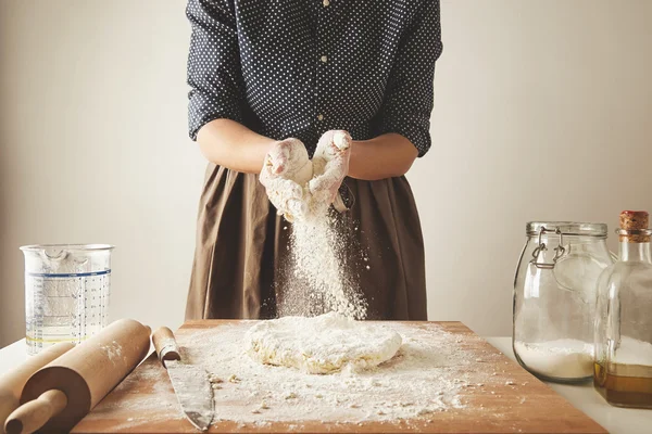 Woman adds some flour to dough on wooden table Лицензионные Стоковые Изображения